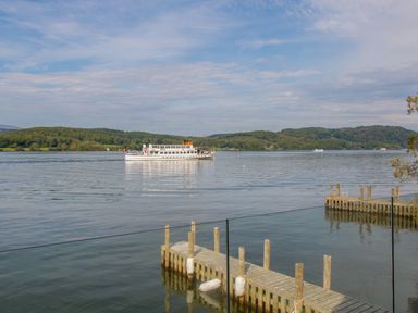 A boat on a lake near wooden docks with forested hills in the background at Boathouse on the Lake in Bowness-On-Windermere