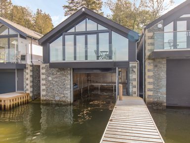 A boathouse with glass balcony and stone walls next to a wooden dock on the water at Boathouse on the Lake in Bowness-On-Windermere