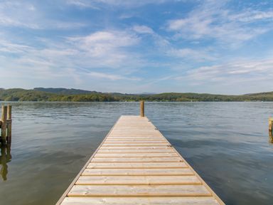 A wooden dock extending over a lake with hills and trees in the background at Boathouse on the Lake in Bowness-On-Windermere