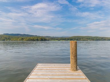 A wooden dock extending into a lake with a wooden post and forested hills in the background at Boathouse on the Lake in Bowness-On-Windermere