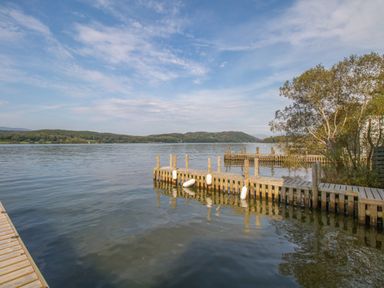 A wooden dock extending into a lake with trees and hills in the background at Boathouse on the Lake in Bowness-On-Windermere