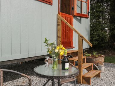 An outdoor seating area with a glass top table holding flowers a wine bottle and an upside down glass near wooden steps and a door at Ewes Welcome in Cottingham