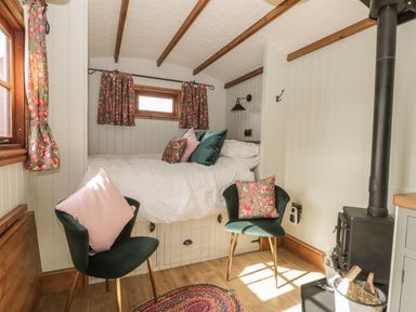 A small bedroom with a bed, two chairs with cushions, floral curtains, a wood-burning stove, and wooden beams at Ewes Welcome in Cottingham