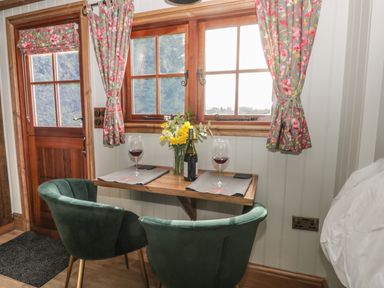 A small dining area with a wooden table set with two wine glasses and a bottle between two green chairs by a window with floral curtains at Ewes Welcome in Cottingham