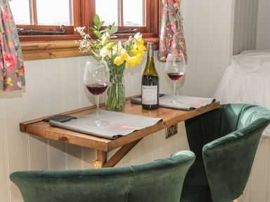 A small wooden table with two green chairs red wine glasses wine bottle and flowers by a window at Ewes Welcome in Cottingham