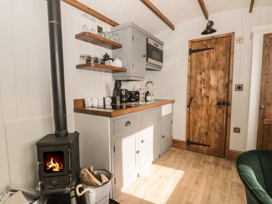 A small kitchen with a wood burning stove mugs jars and a wooden door at Ewes Welcome in Cottingham
