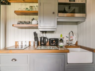 A kitchen with grey cabinets a wooden countertop a white sink a microwave kettle toaster and cups at Ewes Welcome in Cottingham