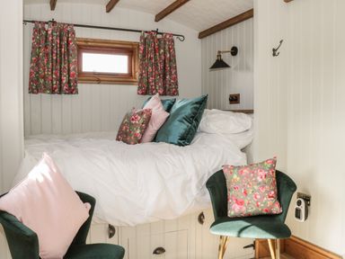 A small bedroom with a bed featuring white bedding and multiple pillows two green chairs with pink and floral cushions and floral curtains at Ewes Welcome in Cottingham