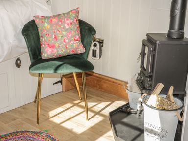 A green chair with a floral cushion next to a black wood stove with a bucket of firewood on a wooden floor at Ewes Welcome in Cottingham