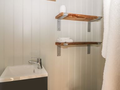 A bathroom corner with a sink and two wooden shelves holding a white vase and towels at Ewes Welcome in Cottingham