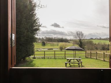 A fenced garden with a picnic table and umbrella overlooking fields and trees at Ewes Welcome in Cottingham
