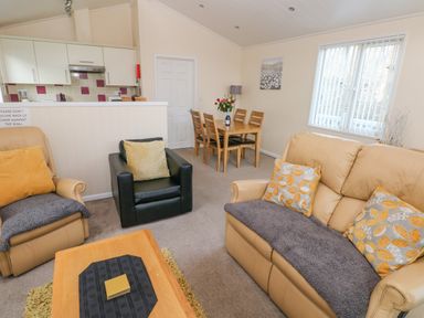 A living room with beige sofa black armchair dining table and kitchen area at The Hideaway - Heritage Park in Stepaside near Kilgetty