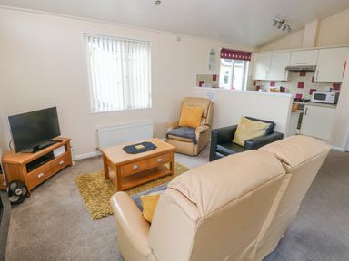 A living area with a beige leather sofa and armchairs a wooden coffee table a television on a wooden stand and an open kitchen at The Hideaway - Heritage Park in Stepaside near Kilgetty