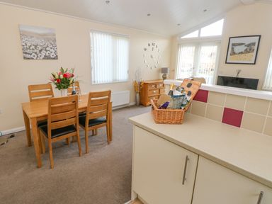 A dining area with wooden table and chairs and a kitchen counter with a basket at The Hideaway - Heritage Park in Stepaside near Kilgetty