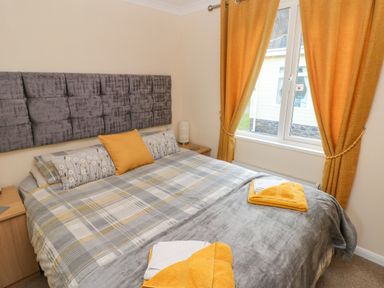 A bedroom with a double bed plaid bedding orange pillows orange curtains and bedside tables at The Hideaway - Heritage Park in Stepaside near Kilgetty