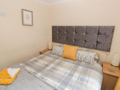 A bedroom with a bed with plaid bedding and yellow cushions and bedside tables with lamps at The Hideaway - Heritage Park Stepaside near Kilgetty