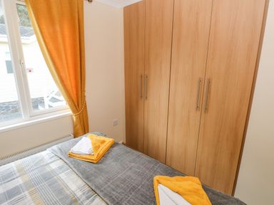 A bedroom with a bed with folded towels on it orange curtains on a window and a wooden wardrobe on the wall at The Hideaway - Heritage Park in Stepaside near Kilgetty
