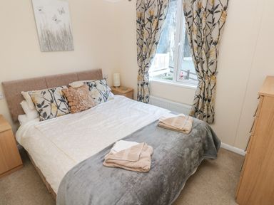 A bedroom with a bed, pillows, folded towels, nightstand, window with curtains, and a dresser at The Hideaway - Heritage Park Stepaside near Kilgetty