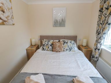 A bedroom with a bed with patterned pillows and bedside tables with lamps near a window at The Hideaway - Heritage Park in Stepaside near Kilgetty