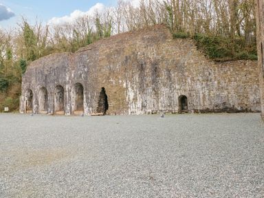 An old stone wall structure with multiple arched openings surrounded by trees at The Hideaway - Heritage Park in Stepaside near Kilgetty