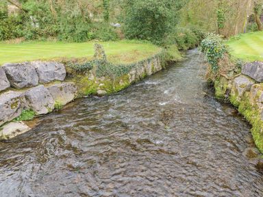 A narrow stream flowing between stone walls with grass and trees on both sides at The Hideaway - Heritage Park in Stepaside near Kilgetty