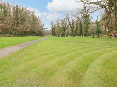 A grassy area with a curved path and trees in the background at The Hideaway - Heritage Park in Stepaside near Kilgetty