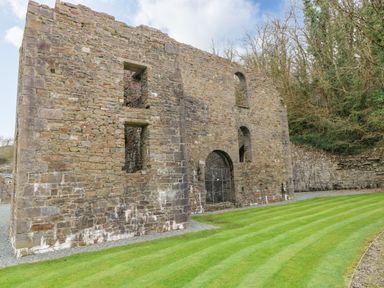 A stone ruin with arched openings and striped grass in front at The Hideaway - Heritage Park in Stepaside near Kilgetty