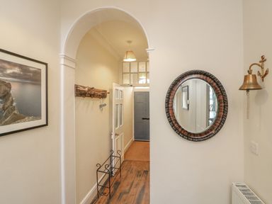 A hallway with a wooden floor a round wall mirror a brass bell a framed picture and a metal shoe rack at Seasides in Weymouth
