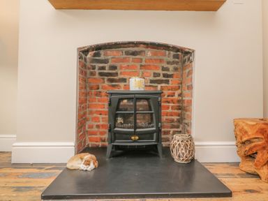 A black stove in a brick fireplace with a candle on top a cat curled up on the hearth and a wicker lantern beside it at Seasides in Weymouth
