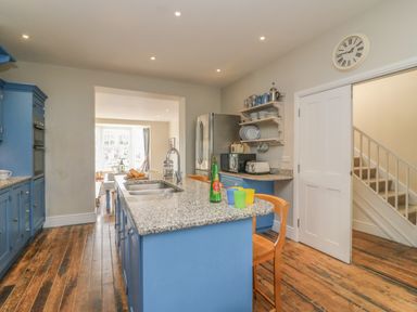 A kitchen with blue cabinets a granite island with sink and chairs a stainless steel fridge and wooden floor at Seasides in Weymouth