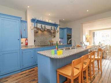 A kitchen with blue cabinets a granite countertop an island with wooden stools and hanging pots and pans at Seasides in Weymouth