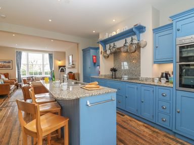 A kitchen with blue cabinets wooden chairs and a living area with leather sofas at Seasides in Weymouth