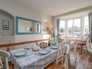 A dining room with a large table set with plates and glasses and a bay window at Seasides in Weymouth