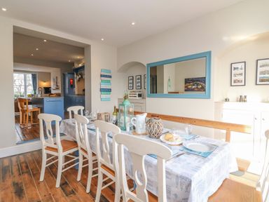 A dining room with a set table and white chairs next to a wooden bench at Seasides in Weymouth