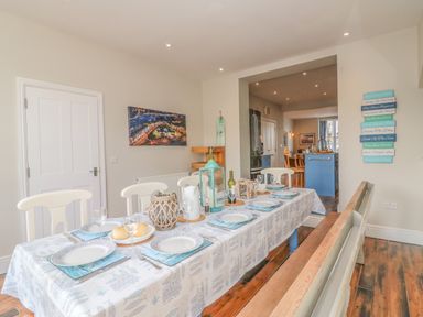 A dining room with a table set for six people with plates glasses and bread at Seasides in Weymouth