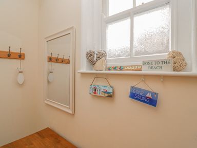 A small corner with a mirror wooden coat rack and window sill decorated with beach-themed signs and ornaments at Seasides in Weymouth