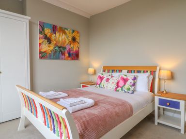 A bedroom with a bed with colorful headboard and footboard floral pillows and bedside tables with lamps at Seasides in Weymouth