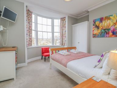 A bedroom with a bed a red chair a white wardrobe and a chest of drawers at Seasides in Weymouth