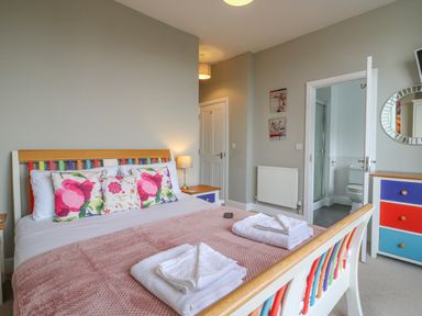 A bedroom with a bed folded towels colorful pillows a dresser and an open door leading to a bathroom at Seasides Weymouth