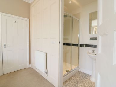 A hallway leading to a bathroom with a glass shower enclosure and pedestal sink at Seasides in Weymouth