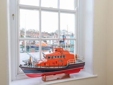 A model lifeboat on a windowsill with a view of boats and buildings outside at Seasides in Weymouth