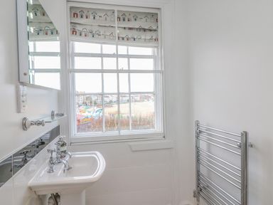 A bathroom with a sink and towel radiator near a window with patterned blinds at Seasides in Weymouth