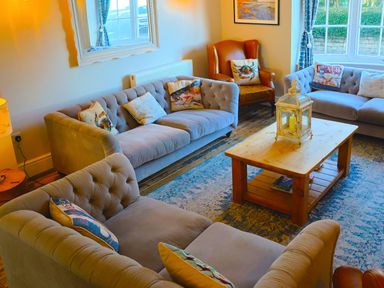 A living room with three sofas a wooden coffee table with lantern a rug and windows at Seasides in Weymouth