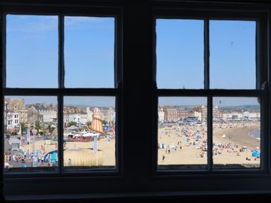 A beach with people and buildings viewed through a window at Seasides in Weymouth