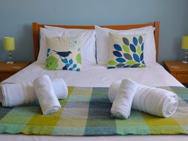 A bed with two decorative pillows and rolled white towels on a checked blanket at Seasides in Weymouth