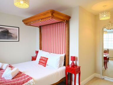 A bedroom with a striped canopy bed red bedside tables and lamps and a large mirror at Seasides Weymouth