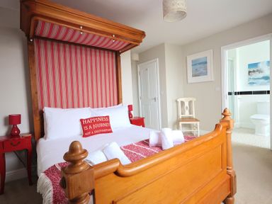 A bedroom with a wooden bed frame red striped headboard red bedside tables and an open door to a bathroom at Seasides Weymouth