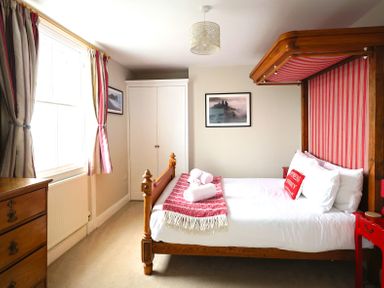 A bedroom with wooden bed frame red striped canopy matching bedside tables and curtains at Seasides in Weymouth