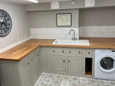 A kitchen corner with grey cabinets wooden countertops a white sink a washing machine a wall clock and a framed map at Seasides in Weymouth