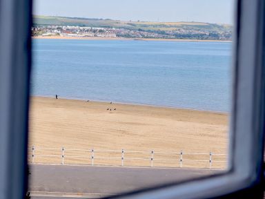 A view of a sandy beach with birds and a blue sea beyond seen through a window at Seasides in Weymouth